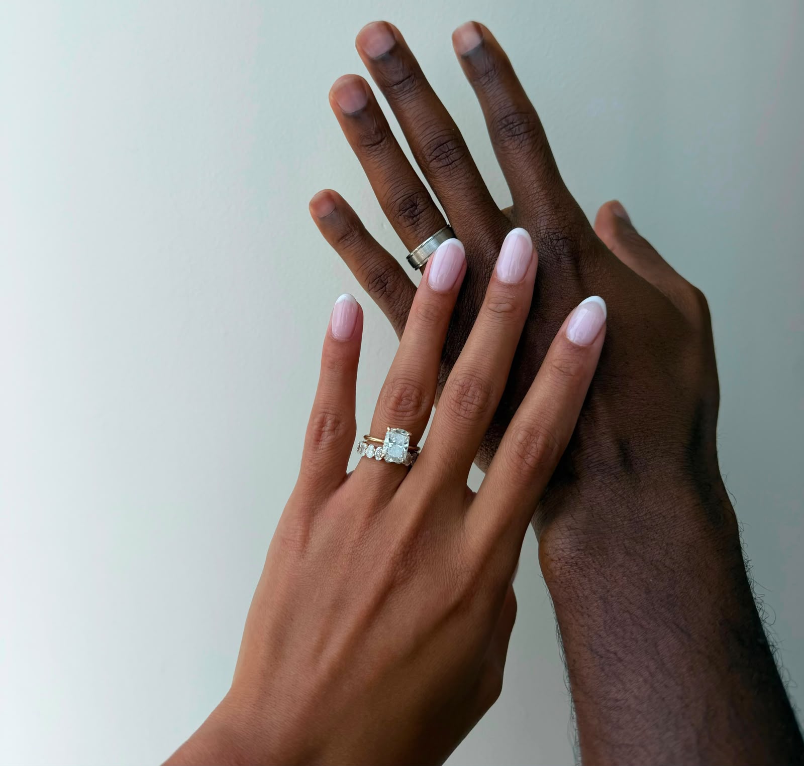 Bride and groom wearing bespoke wedding rings, including an oval diamond engagement ring, a 3ct oval eternity band and a 5mm grooved platinum band.
