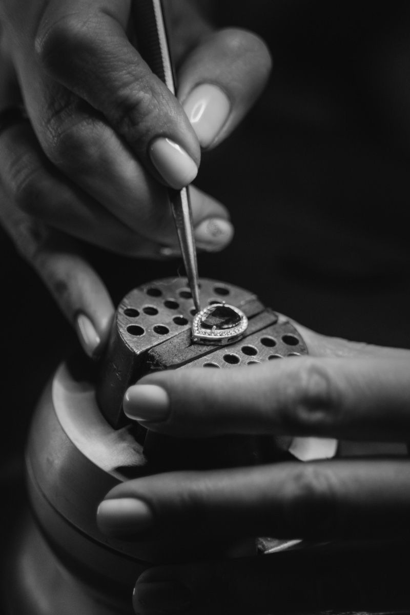 Jeweller hand-setting stones into a bespoke halo engagement ring at the workbench.
